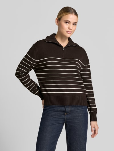 Frauenmodel trägt Regular Fit Pullover aus reiner Baumwolle von MANGO in Dunkelbraun mit weißen Streifen, Strick-Optik, Troyer-Kragen, elastische Abschlüsse, Ganzkörperansicht von vorne.