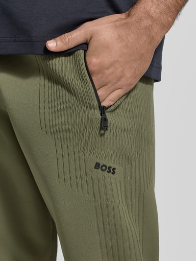 Mężczyzna nosi Regular Fit Sweatpants mit Jacquard Akzenten Modell 'ACTIVE PUSH' od BOSS Green, detal z bliska, gładka faktura, zamek kieszeni.