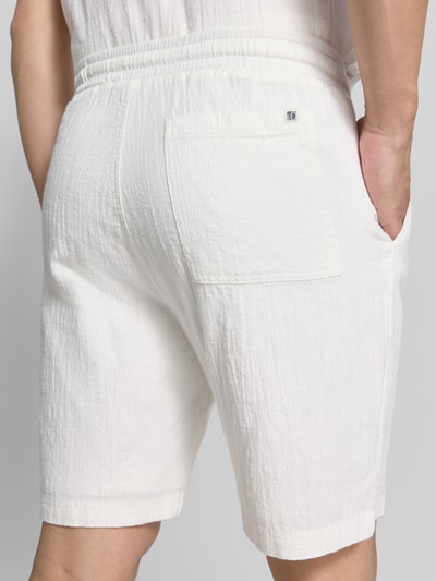 Männermodel trägt Relaxed Fit Stoffshorts aus einer Baumwolle von s.Oliver RED LABEL in Weiß, strukturierte Oberfläche, Ganzkörperansicht Rückansicht.