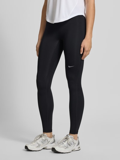 Frauenmodel trägt Leggings mit Logo und elastischem Bund von NIKE TRAINING, schwarzer Material-Mix mit Stretch-Anteil, körpernahe Passform, Nahaufnahme Unterkörper.