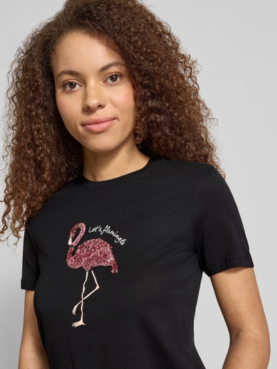 Modelka kobieca ma na sobie Regular Fit T-Shirt aus reiner Baumwolle Modell 'KITA' od Only w kolorze czarnym z nadrukiem flaminga i cekinami, okrągły dekolt, krótki rękaw, bawełniany jersey, widok na górną część ciała z przodu.