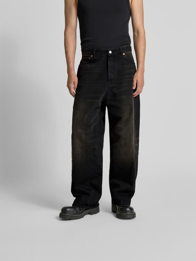 Männermodel trägt weite schwarze Jeans mit leichter Washed-Optik, grobe Textur, Five-Pocket-Design, Ganzkörperansicht von vorne.