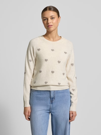 Vrouwenmodel draagt Regular Fit gebreide pullover met intarsia model 'DOFFY INTARSIA' van Vero Moda, effen kleur, all-over motief, labelstitching applicatie, ronde hals, lange mouwen, geribde mouwboord en rompzoom, materiaalverwerking: knitwear, voorkant bovenlichaam close-up.
