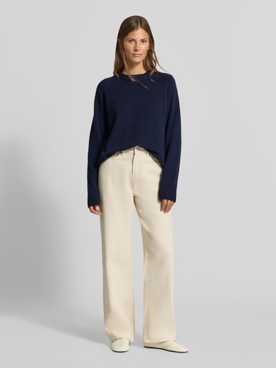 Frauenmodel trägt Regular Fit Pullover aus reinem Kaschmir in Strick-Optik von MYON, dunkelblau, kombiniert mit heller Hose, Rundhalsausschnitt und langen Ärmeln, Ganzkörperansicht von vorne.