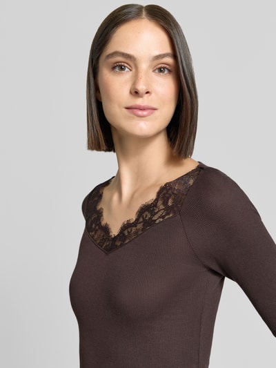 Frauenmodel trägt Slim Fit Longsleeve aus reiner Baumwolle von Rich & Royal in Dunkelbraun mit Spitzenbesatz und V-Ausschnitt, Nahaufnahme Oberkörper.