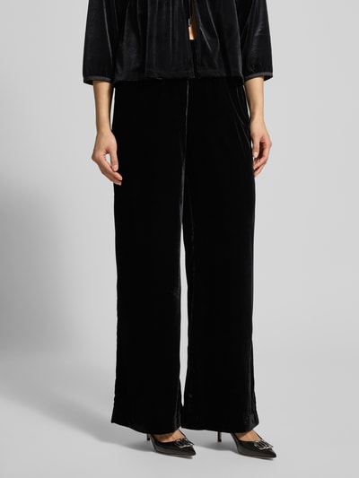 Kobiece modelka nosi spodnie materiałowe z elastycznym pasem OPUS PANTS, model 'Mucia', czarne, luźny krój, wpuszczane kieszenie, widok z przodu, ujęcie całej sylwetki.