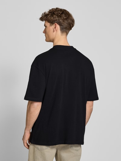 Männermodel trägt Oversized Herren T-Shirt von Pegador aus Reine Baumwolle, schwarze Farbe, 1/2-Arm, Rückenlänge 70 cm, Modell 'Signar', Ganzkörperansicht Rückansicht.