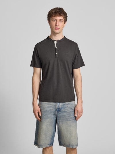 Männermodel trägt T-Shirt mit kurzer Knopfleiste von Superdry in dunklem Ton, Regular-Fit aus Leinen-Baumwoll-Mix mit Polokragen, Logo-Stitching, Rückenlänge bei Größe M 62 cm, Ganzkörperansicht von vorne.