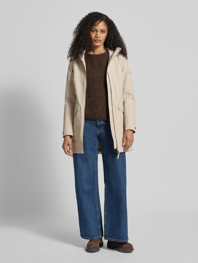 Frauenmodel trägt Regular Fit Parka mit Logo-Applikation Modell 'Folka' von Didriksons in Beige mit Stehkragen, Kapuze, Zweiwege-Reißverschluss, aufgesetzten Taschen, sichtbare Struktur, Rückenlänge 83 cm, Schulterbreite 40 cm, Brustweite 46 cm, Ärmellänge 64 cm, Ganzkörperansicht von vorne.