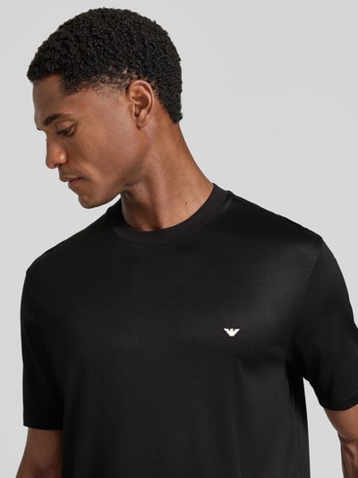 Männermodel trägt T-Shirt aus Lyocell-Mix mit Label-Stitching von Emporio Armani, schwarze Farbe, glatte Textur, Nahaufnahme Oberkörper.