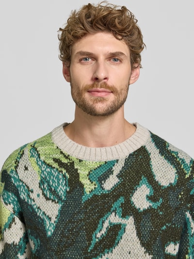 Männermodel trägt Regular Fit Strickpullover mit Baumwoll-Anteil von Scotch & Soda, farbig gemustert, Nahaufnahme Oberkörper. Material-Mix, gerippte Abschlüsse, Rundhalsausschnitt, langärmliges Design.