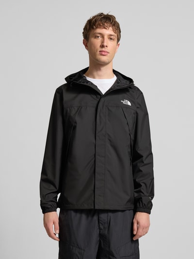 Męski model nosi kurtkę z logo model 'ANTORA' od The North Face, czarny kolor, krój regular fit, kaptur z tunelem, zamek błyskawiczny, długość tyłu w rozmiarze M: 74 cm, szerokość ramion w rozmiarze M: 46 cm, szerokość klatki piersiowej w rozmiarze M: 58 cm, długość rękawów w rozmiarze M: 69 cm, widok całej sylwetki z przodu.