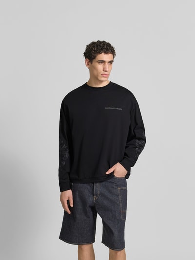 Männermodel trägt Oversized Sweatshirt aus Baumwolle von Don’t Waste Culture, schwarze Farbe, Florale-Stickereien, elastische Abschlüsse, Rundhalsausschnitt, Reine Baumwolle, Rückenlänge 66 cm bei Größe M, Ganzkörperansicht von vorne.