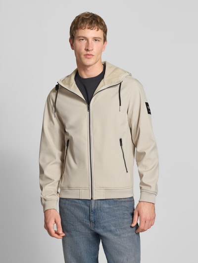 Männermodel trägt Softshelljacke mit Reißverschlusstaschen von Jack & Jones in Beige, Regular-Fit, Kapuze mit Tunnelzug, Ganzkörperansicht von vorne. Rückenlänge bei Größe M 59 cm, Schulterbreite 39 cm, Brustweite 48 cm, Ärmellänge 62 cm.