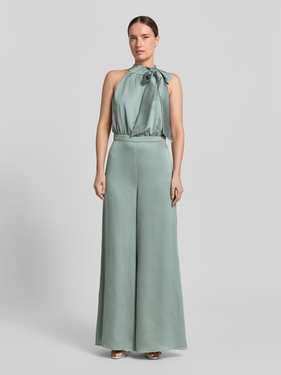 Modelka kobieca ma na sobie Jumpsuit mit Schluppe und rückseitigem Knopfverschluss od Swing, satyna, krój slim fit, kolor pastelowozielony, całkowita długość 152 cm, długość wewnętrzna nogawki 82 cm, szerokość w rozmiarze 36: 66 cm, z tyłu zapięcie na guzik oraz zatrzask i zamek, widok całej sylwetki z przodu.