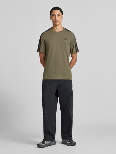 Männermodel trägt olivgrünes Regular Fit T-Shirt aus reiner Baumwolle Modell 'M 3S SJ LC T' von adidas Sportswear, Ganzkörperansicht von vorne.