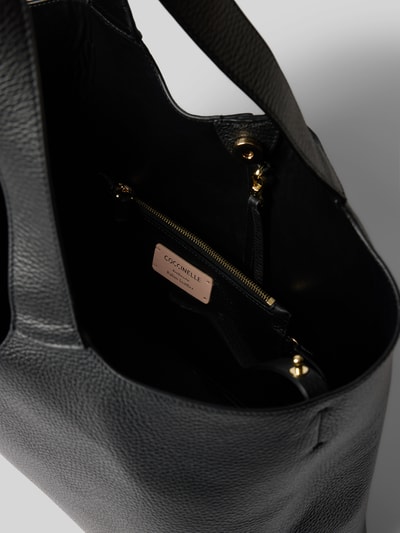 Produktfoto, Tote Bag mit Logo-Detail von Coccinelle in Schwarz, sichtbare strukturierte Oberfläche, herausnehmbare Innentasche, goldfarbene Details, Magnetverschluss, Innensicht Hauptfach, Damen Tote Bag von Coccinelle, Hauptfach mit Magnetverschluss, herausnehmbare Innentasche