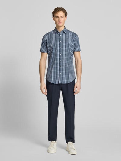 Męski model nosi Slim Fit Business-Hemd aus Baumwolle mit Kentkragen od Jake*s, błękitno-granatowa krata, krój slim fit, czysta bawełna, kołnierzyk kent, krótki rękaw, długość pleców w rozmiarze 39/40: 79 cm, szerokość ramion w rozmiarze 39/40: 48 cm, długość rękawa w rozmiarze 39/40: 23 cm, pełny widok z przodu.
