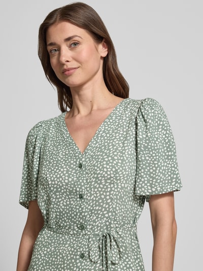 Kobiece modelka nosi Leicht ausgestelltes Minikleid aus reiner Viskose Modell 'ALBA' od Vero Moda, zielony w białe kropki, krótki rękaw, dekolt V, pasek w talii, mini długość, wizkoza, jednolity wzór, widok zbliżeniowy na górną część ciała.