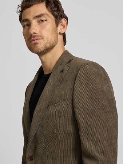 Männermodel trägt Sakko mit Pattentaschen und Reverskragen Modell 'Theo' von Carl Gross aus braunem Cord, Nahaufnahme Oberkörper. Regular Fit, sichtbare Knopfleiste und Brustleistentasche mit Einstecktuch, strukturierte Oberfläche.