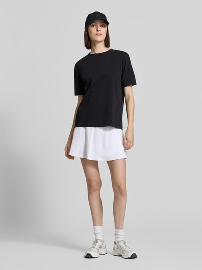 Kobiece modelka nosi 'Eng anliegender Sport Mini-Rock mit Logo Bund' od Lacoste Sport, biały kolor, gładka faktura, krój regular fit, mini długość, elastyczny pas z logo, materiał piqué z technologią Ultra-Dry, widok całej sylwetki z przodu.