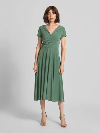 Frauenmodel trägt Tailliertes Cocktailkleid mit V-Ausschnitt von Vera Mont in mattem Grün mit feiner Struktur, Ganzkörperansicht von vorne.