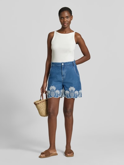 Frauenmodel trägt Shorts mit Lochstickerei Modell 'PILAR' von Guess in Blau aus Reine Baumwolle, Wide-Fit, Eingrifftaschen, Ganzkörperansicht von vorne.