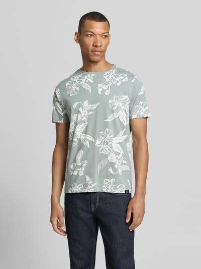 Męski model nosi T-Shirt mit Rundhalsausschnitt und Label-Detail von Lerros, zielony wzór kwiatowy, bawełna, prosty krój, okrągły dekolt, detal z logo, długość tyłu w rozmiarze M: 70 cm, Ganzkörperansicht von vorne.