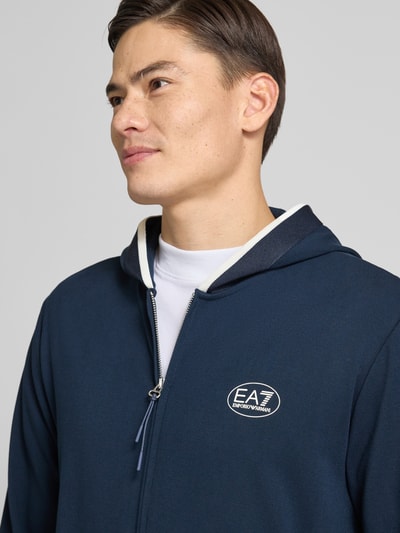 Męski model nosi bluza rozpinana z logo i zamkiem błyskawicznym dwustronnym od Armani, mieszanka wiskozy, krój regular fit, wpuszczane kieszenie, kaptur. Nahaufnahme oberkörper.
