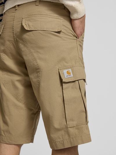 Męski model nosi Shorts mit Cargotaschen od Carhartt Work In Progress, jasnobeżowy krój regular fit, tekstura ripstop, tylne i cargo kieszenie, Szerokość w rozmiarze 32: 43 cm, długość nogawki od wewnątrz: 29 cm, zbliżenie na tył.
