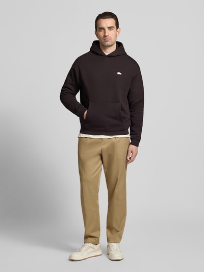 Männermodel trägt Regular Fit Hoodie aus reiner Baumwolle von Lacoste, Optik: Unifarben, Motiv-Print, Langarm, Sweat, Ganzkörperansicht von vorne.