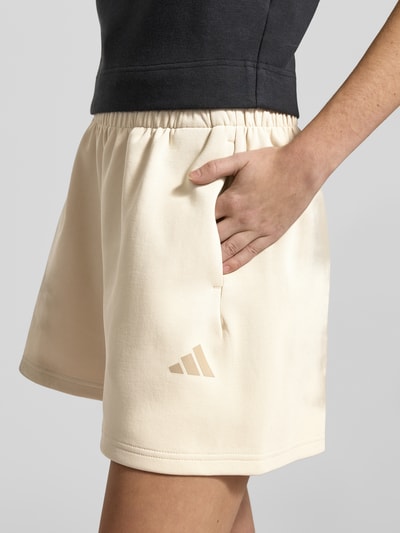 Frauenmodel trägt Shorts mit elastischem Bund von adidas Sportswear in Beige, lockerer Schnitt, Label-Print, Nahaufnahme Oberschenkel.
