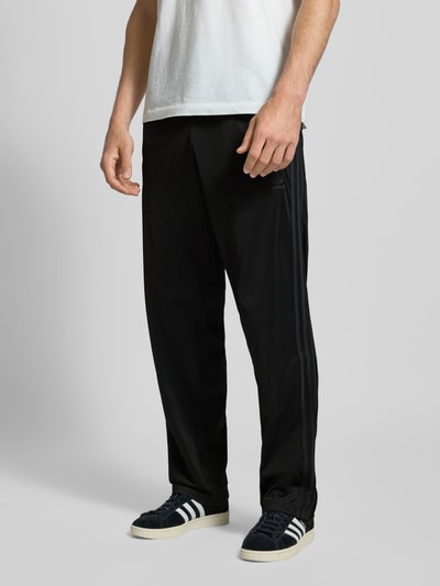 Männermodel trägt schwarze Trainingshose mit elastischem Bund Modell 'FIREBIRD' von adidas Originals, Regular Fit, Ganzkörperansicht von vorne.