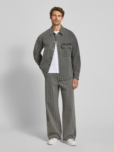 Männermodel trägt Regular Fit Hemdjacke aus reiner Baumwolle Modell 'David' von Wood Wood, Denim-Optik, Grau mit Streifen, Ganzkörperansicht von vorne.