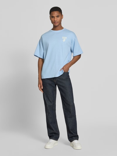 Männermodel trägt ein hellblaues Relaxed Fit T-Shirt mit weißem Statement-Print von Casual Friday, reine Baumwolle, Ganzkörperansicht von vorne.