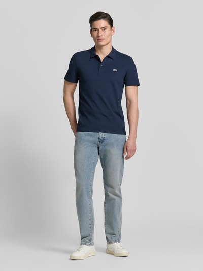 Männermodel trägt Regular Fit Poloshirt aus Baumwoll-Mix von Lacoste in Optik: Unifarben, Logo-Patch, Kragenform: Polokragen, Ärmelform: Kurzarm, Ganzkörperansicht von vorne.
