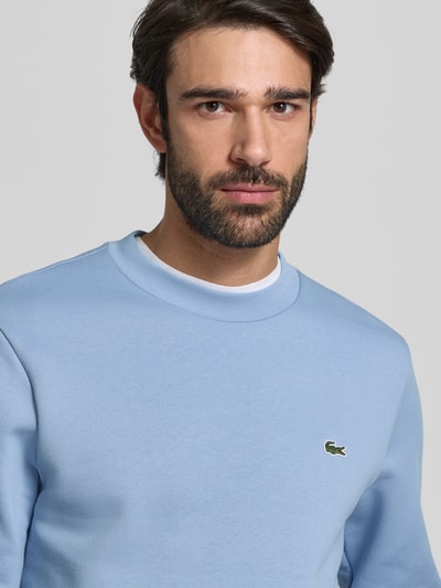 Męski model nosi Classic Fit Sweatshirt aus Baumwoll-Mix od Lacoste, efekt: jednolity kolor, wyhaftowane logo; mieszanka bawełny, niebieska bluza, okrągły dekolt, długi rękaw, widok z przodu, zbliżenie na górną część ciała.