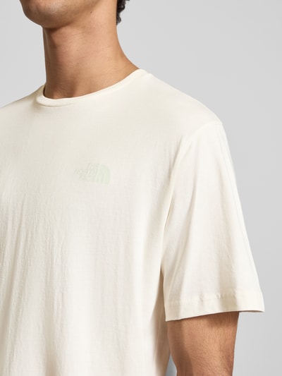 Männermodel trägt T-Shirt mit Label-Print von The North Face in Creme, Reine Baumwolle, Regular-Fit, gerippter Rundhalsausschnitt, Nahaufnahme Oberkörper.