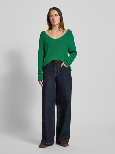 Frauenmodel trägt Regular Fit Strickpullover aus reiner Baumwolle von Tommy Hilfiger, zielony, paski, logo, długi raglanowy rękaw, dekolt V, bawełna, przód, całopostaciowe ujęcie.