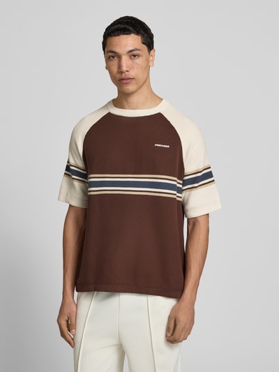 Męski model nosi Strickshirt mit Label-Stitching und Rundhalsausschnitt von Pegador z bawełny, krój regular fit, model 'Eger Pique', długość tyłu w rozmiarze M: 65 cm, kolor brązowo-kremowy z paskami, widok całej sylwetki od przodu.