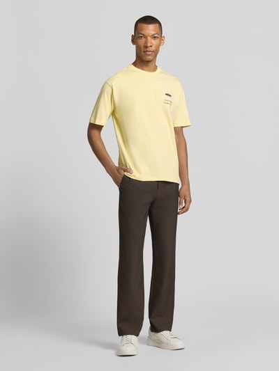 Männermodel trägt T-Shirt mit rückseitigem Motiv-Print von MCNEAL in Gelb, aus Bio-Baumwolle, gerade geschnitten, Ganzkörperansicht von vorne.