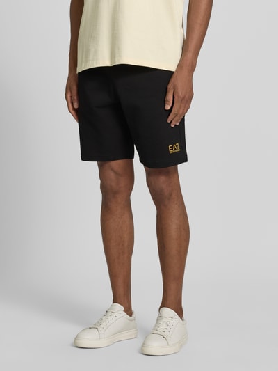 Männermodel trägt schwarze Shorts mit elastischem Bund und Logo von EA7 Emporio Armani aus Reine Baumwolle, Regular-Fit, Nahaufnahme Oberkörper.