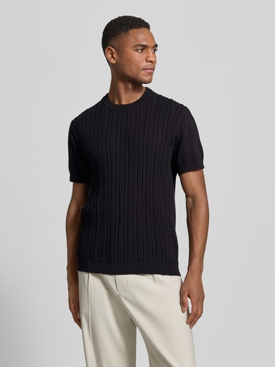 Männermodel trägt T-Shirt mit Zopfmuster von Lindbergh in Schwarz, reine Baumwolle, gerader Schnitt, Strick-Optik, Ganzkörperansicht von vorne.