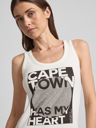 Frauenmodel trägt Slim Fit Top mit Strasssteinbesatz Modell 'Cape Town' von monari, weiß, schwarzer Statement-Print, Nahaufnahme Oberkörper.