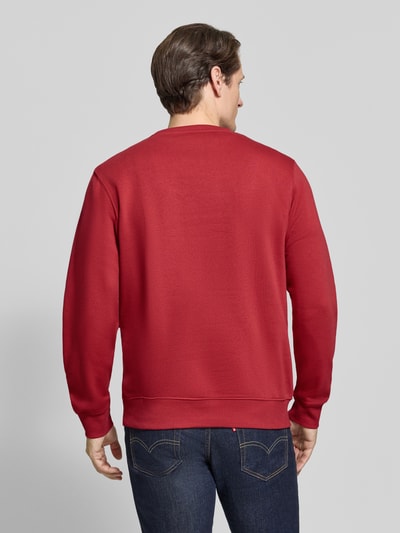 Männermodel trägt Regular Fit Sweatshirt aus Baumwoll-Mix von LERROS in Rot, glatte Struktur, Jeans kombiniert, Ganzkörperansicht Rückansicht. Rückenlänge bei Größe M 67 cm, Ärmel 65 cm, gerippte Abschlüsse, Logo-Patch sichtbar.