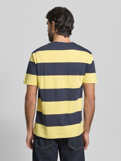 Männermodel trägt Regular Fit T-Shirt mit Logo-Print Modell 'BAR' von Gant, reine Baumwolle, breite gelbe und dunkelblaue Streifen, Ganzkörperansicht Rückansicht.