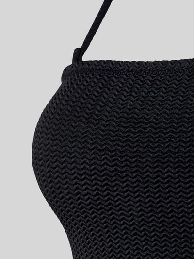 Frauenmodel trägt Body mit Neckholder von Seafolly in Schwarz, feine Wellenstruktur und Stretch-Material, Nahaufnahme Oberkörper.