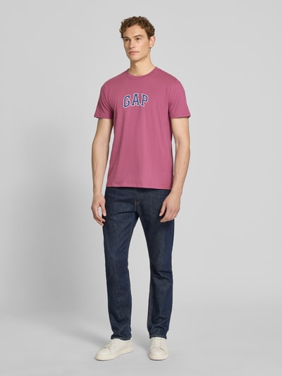 Männermodel trägt T-Shirt mit Logo-Patch und Rundhalsausschnitt von GAP in Rosa aus reiner Baumwolle, Straight Fit, Ganzkörperansicht von vorne.