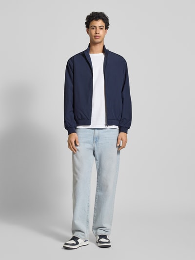 Männermodel trägt Regular Fit Jacke mit Stehkragen Modell 'Charge' von JACK & JONES in Dunkelblau, Reißverschluss, Eingrifftaschen, elastische Abschlüsse, Ganzkörperansicht von vorne.