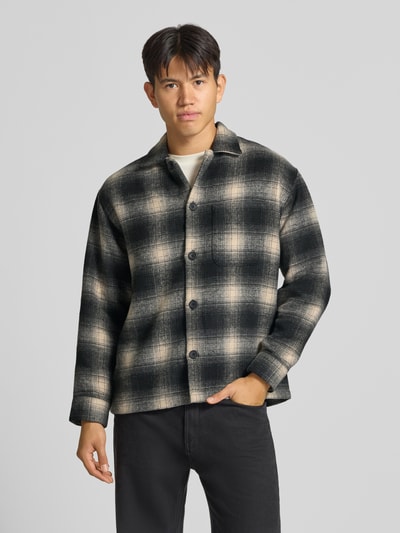 Männermodel trägt Regular Fit Hemdjacke mit Brusttasche Modell 'SOHO OLLIE' von JACK & JONES in Schwarz-Beige-Karo, Ganzkörperansicht von vorne. Herren Hemdjacke mit Kentkragen, durchgehender Knopfleiste, mittlerer Rückenlänge, schmaler Schulterbreite und langen Ärmeln.